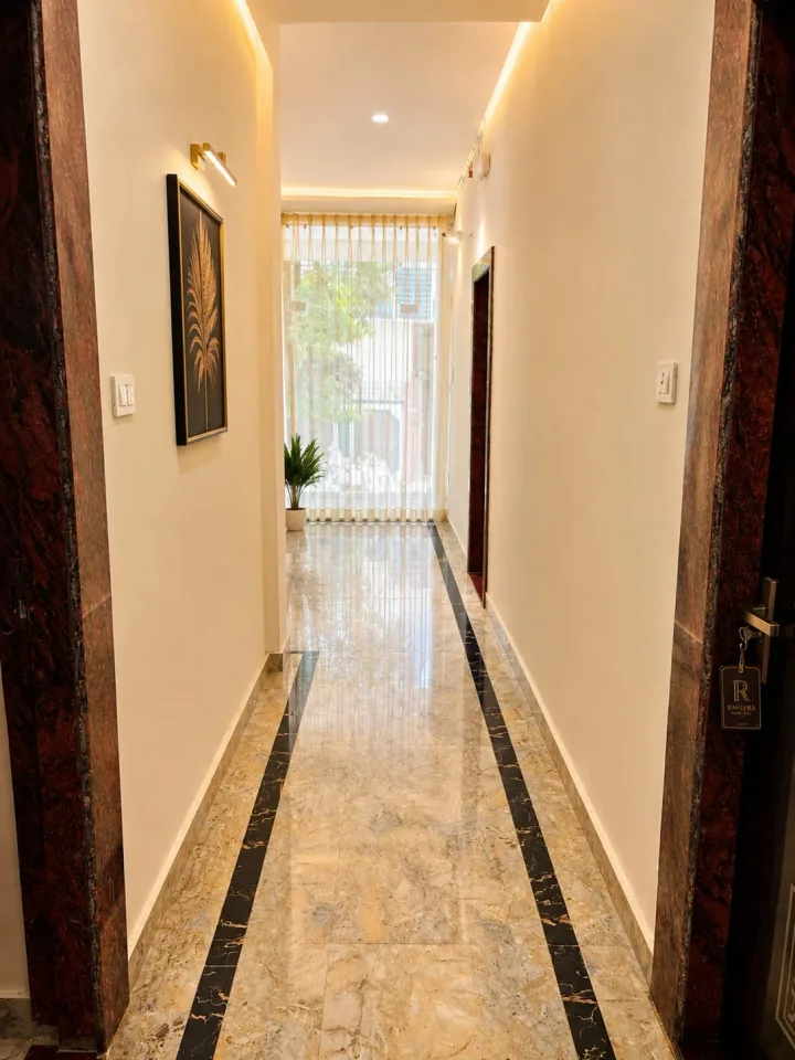 Guest room corridor with polished marble tile flooring, recessed cove lighting, and natural window light