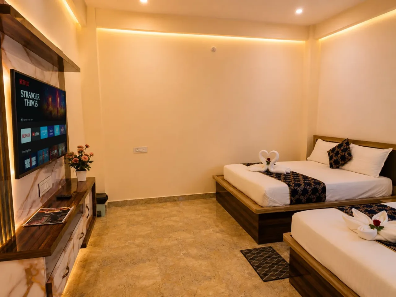 Air-conditioned guest bedroom suite with twin queen beds, polished marble flooring, smart LED TV console, and decorative swan towel art