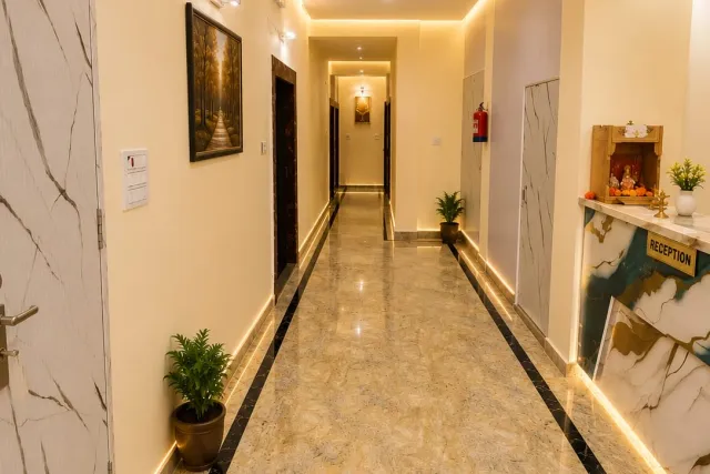 Bright reception corridor with polished marble-look flooring, brass front desk, mandir, and cove LED lighting