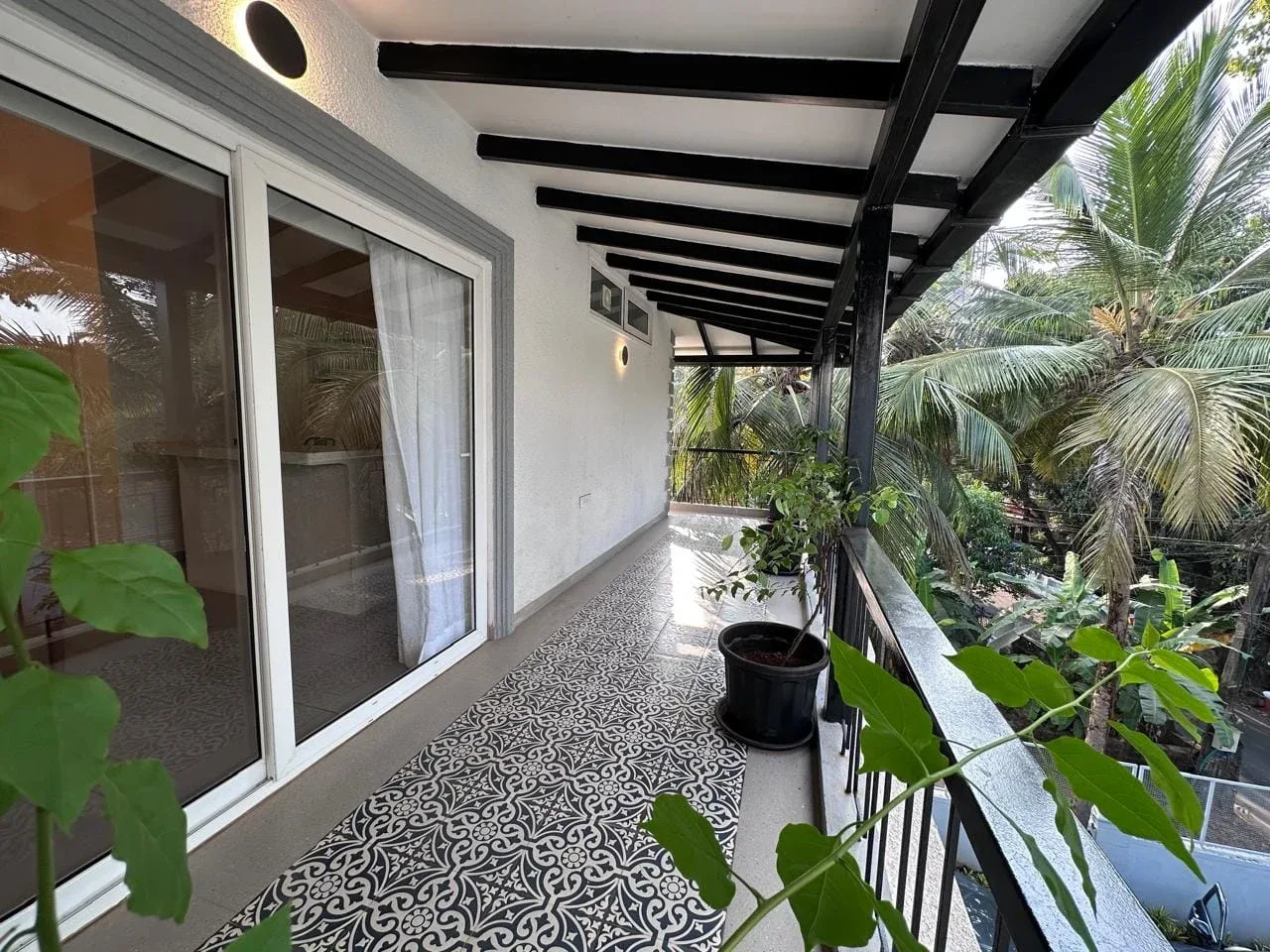 Deep covered veranda balcony with traditional Goan patterned floor tiles and tropical palm canopy views