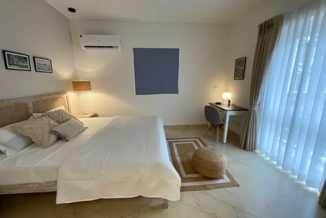 Spacious ground-floor bedroom suite with reading lamp, jute rug, and pouf