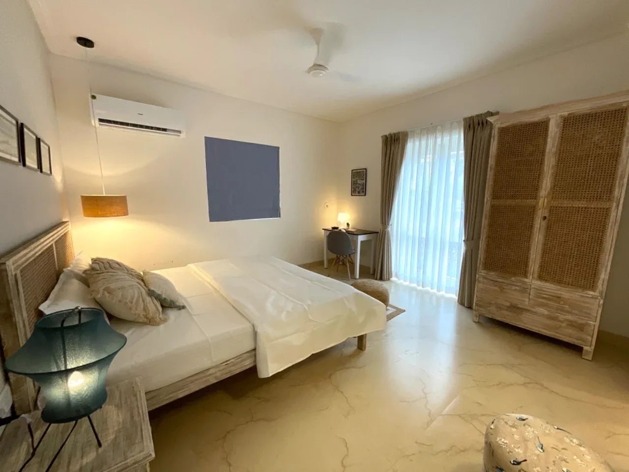 Ground-floor bedroom suite with study desk, cane wardrobe, and floor-to-ceiling balcony doors